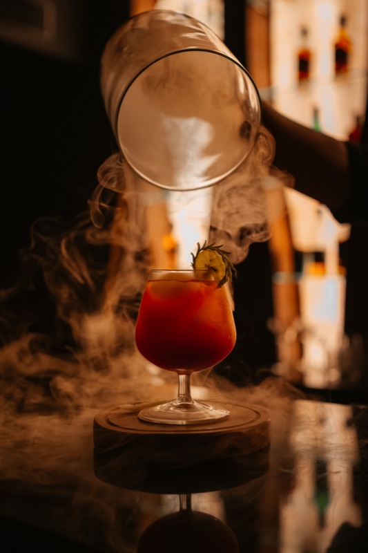 A glass cloche lifted off a red cocktail at the Bellers bar, smoke spilling over the black bar top