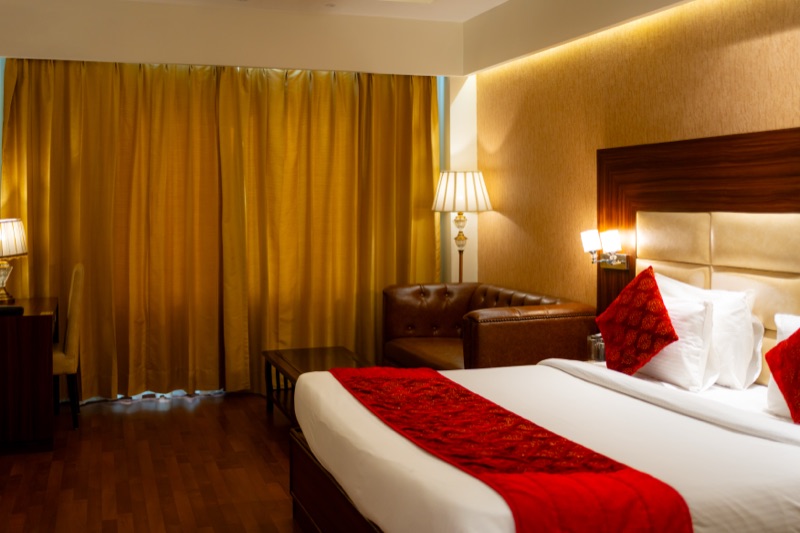 A double room made up: a red runner and cushions on the bed, the bedside lamps on, gold curtains