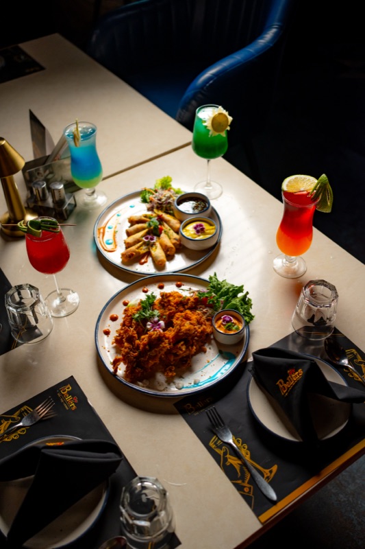 A table spread from above: two plated dishes and four colourful drinks on Bellers placemats