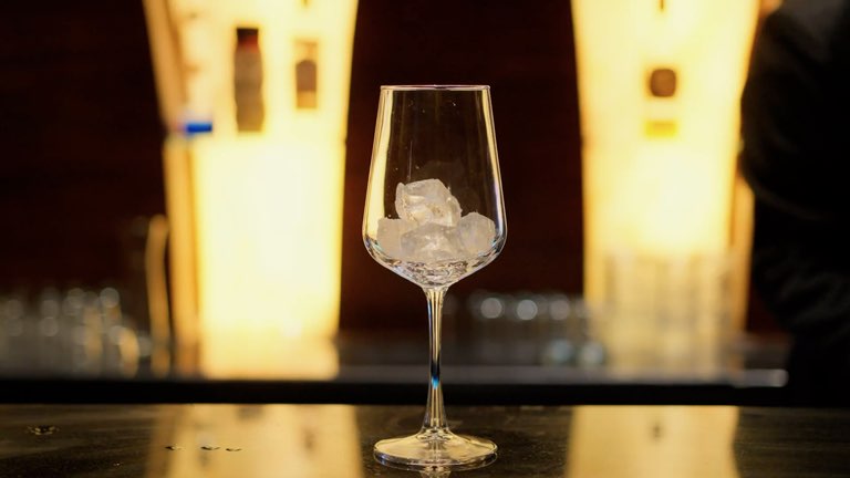Film: a bartender pours a blue drink over ice into a wine glass at the Bellers bar, the lit bottle wall behind