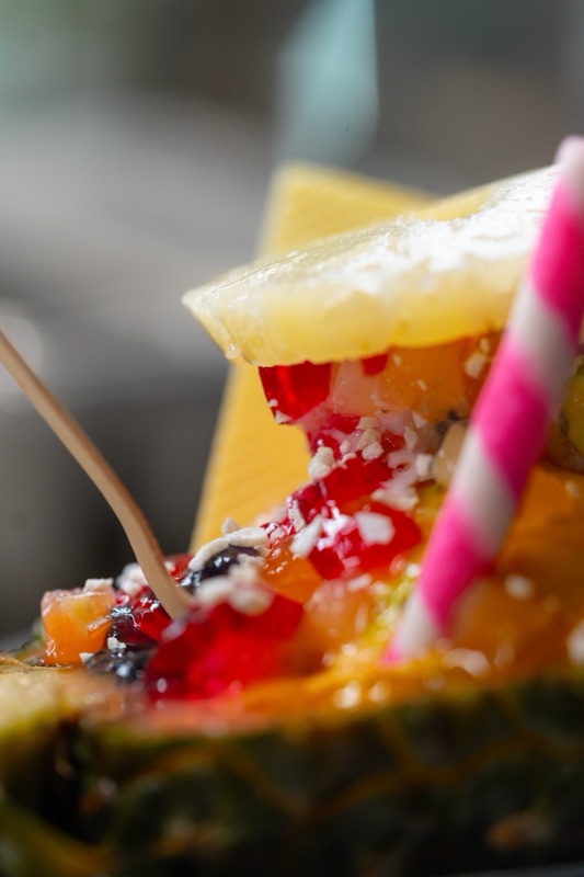 A fruit sundae served in half a pineapple, with coconut flakes and a pink striped straw
