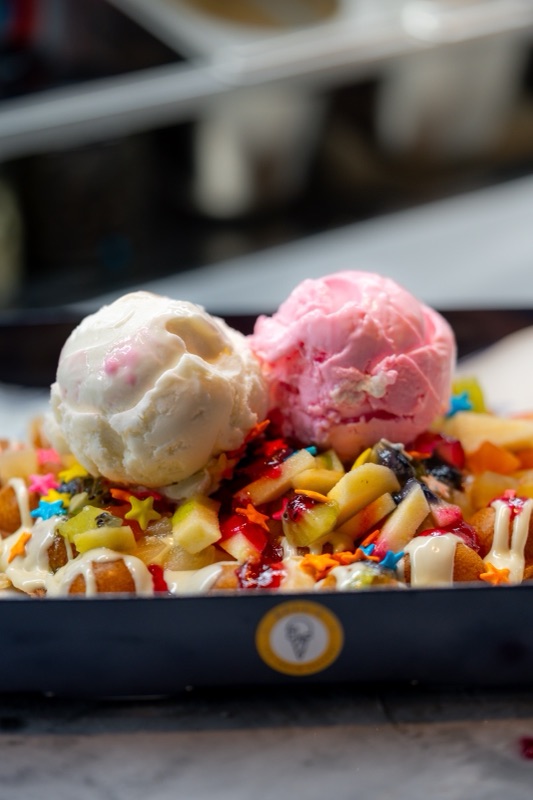 A waffle loaded with fruit, sauces and two scoops, in a Bell’s box