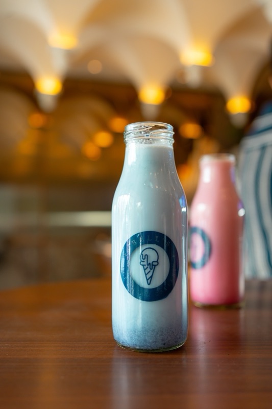 Blue and pink shakes in Bell’s own glass bottles, the shop’s vaulted ceiling glowing behind