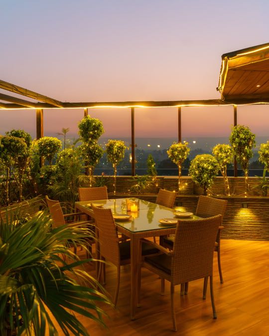 The rooftop terrace at The Grand Ambassador at sunset: a table laid under string lights, plants all round and the sky going pink
