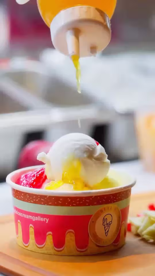 A fresh fruit sundae being made at Bell’s Ice Cream Gallery: mango sauce poured over the scoops in a pink Bell’s cup