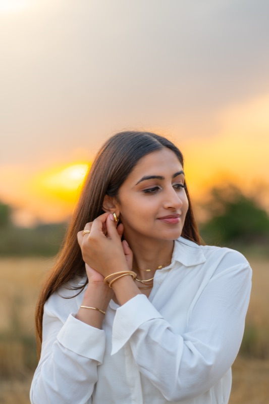 A model touching her earring in a field at golden hour, for Nuve