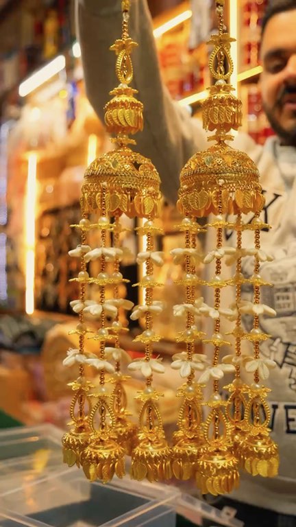 Gold bridal kaleere swinging in front of the lit shelves at Prem Di Hatti