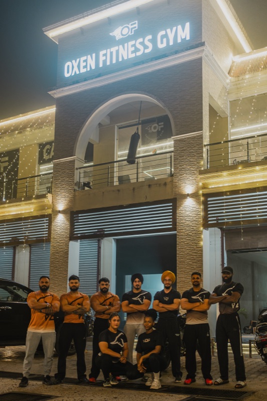 The Oxen Fitness coaching team in matching tees in front of the lit gym sign at night