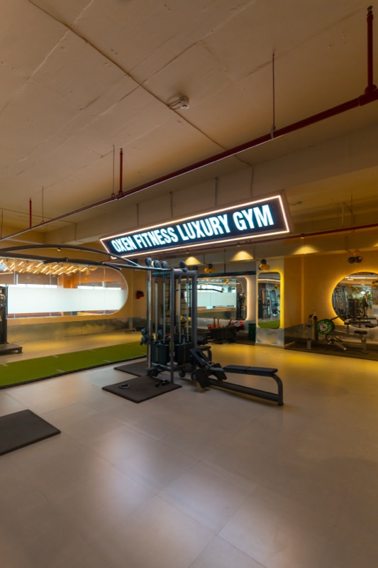 The gym floor at Oxen: a cable machine and a bench under the lit &lsquo;Oxen Fitness Luxury Gym&rsquo; sign