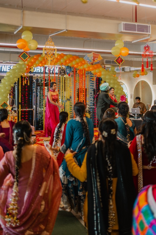 Teej at the gym: women in bright suits and dupattas, a stage under a balloon arch and marigold strings