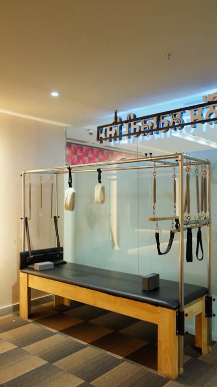Reel: a coach spotting and adjusting a member on the Pilates equipment