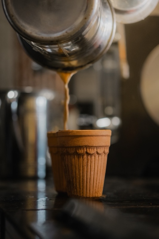 Chai poured from a steel pot into a clay kulhad
