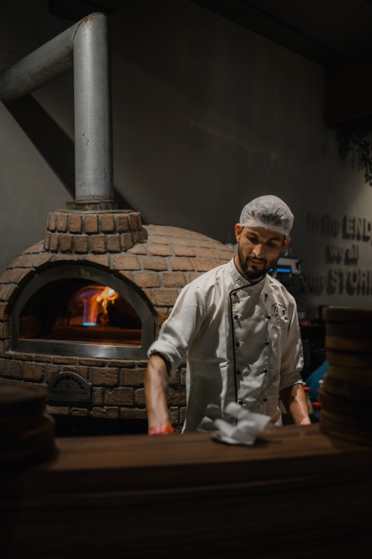 A chef at the counter in front of a wood-fired pizza oven