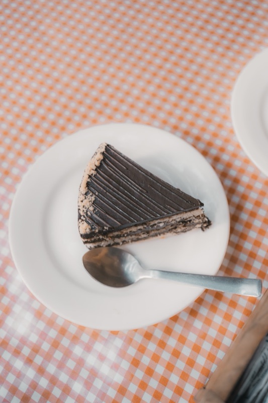 A slice of layered chocolate cake with a spoon, on an orange gingham cloth