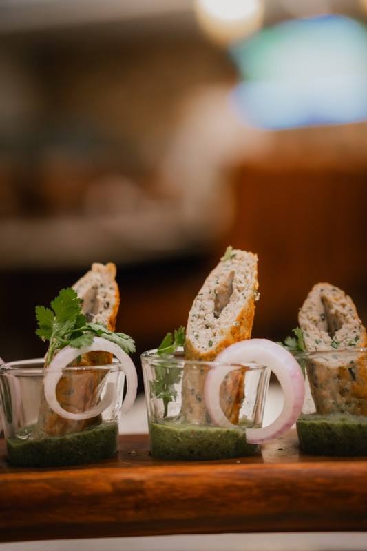 Stuffed rolls standing in small glasses of green chutney, with onion rings, on a wooden board