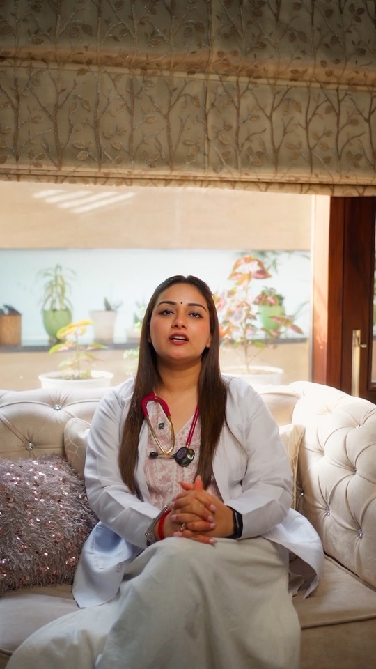 Dr Bedi in a white coat on a white sofa by a bright window